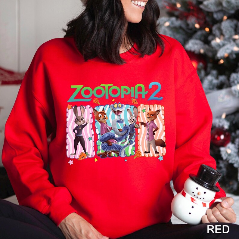 May include: A red sweatshirt featuring the text "ZOOTOPIA 2" in green and a graphic of characters from the movie. The graphic includes a rabbit, fox, and other characters in colorful outfits. The word "RED" is printed in white at the bottom right.