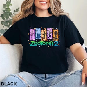 May include: Black t-shirt featuring a colorful graphic of characters from Zootopia 2. The design includes images of a fox, a rabbit, and other animals in rectangular frames. The text "Zootopia 2" is in green and blue.