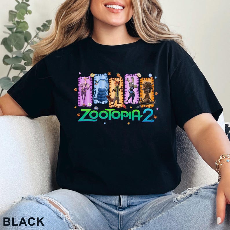 May include: Black t-shirt featuring a colorful graphic of characters from Zootopia 2. The design includes images of a fox, a rabbit, and other animals in rectangular frames. The text "Zootopia 2" is in green and blue.
