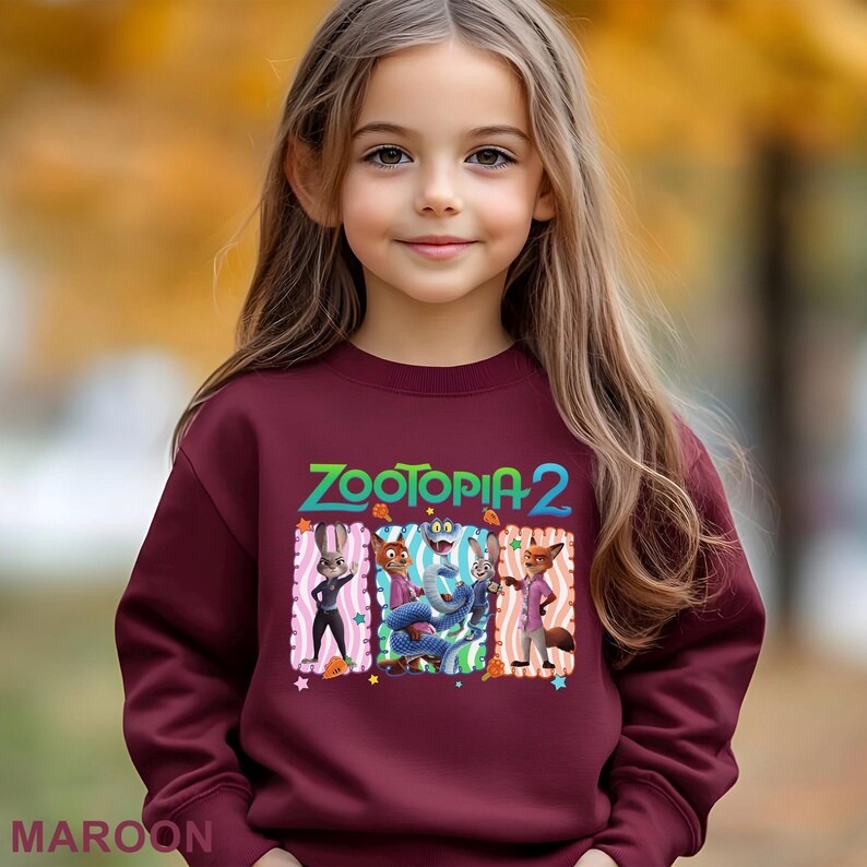 May include: A maroon sweatshirt featuring the text "ZOOTOPIA 2" in green, blue, and orange. The graphic includes cartoon characters from the movie. The word "MAROON" is printed at the bottom of the sweatshirt.