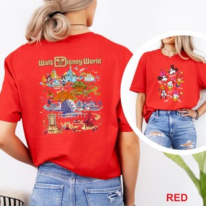 Op de afbeelding: Rood t-shirt met een kleurrijke afbeelding van Disney World attracties en personages. De achterkant van het shirt toont de woorden "Walt Disney World" boven een gedetailleerde illustratie van het park. De voorkant van het shirt heeft een afbeelding van Disney-personages.