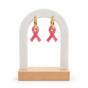 Peut inclure: Une paire de boucles d'oreilles créoles dorées avec des breloques en forme de ruban rose. Chaque boucle se compose d'un anneau circulaire doré poli avec un petit pendentif en forme de ruban de sensibilisation rose translucide.