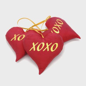 May include: Four red heart-shaped decorations with yellow text reading "XO XO". Each heart has a yellow ribbon for hanging. The ornaments are made of a soft fabric.