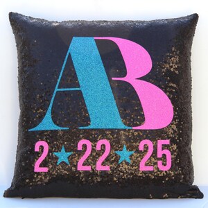 May include: Black sequin pillow with the letters "AB" in turquoise and pink, and the numbers "2 22 25" in pink.