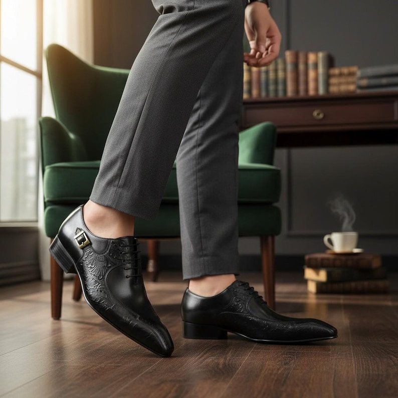Pu&ograve; includere: Scarpe eleganti in pelle nera con intricati motivi floreali in rilievo. Le scarpe hanno una punta affilata, un piccolo tacco e una fibbia. Sono indossate con pantaloni grigi.