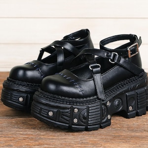 Puede incluir: Par de zapatos Mary Jane con plataforma negros. Estos zapatos presentan una suela de plataforma gruesa con tachuelas y hebillas metálicas decorativas. Las partes superiores tienen un diseño de correas con detalles de costura.