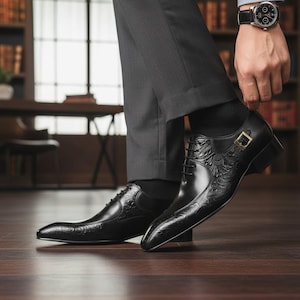Pu&ograve; includere: Scarpe eleganti in pelle nera con dettagli floreali e a foglie in rilievo. Le scarpe presentano una punta affusolata, chiusura con lacci e fibbia color oro. Indossate con calzini neri e pantaloni grigi.