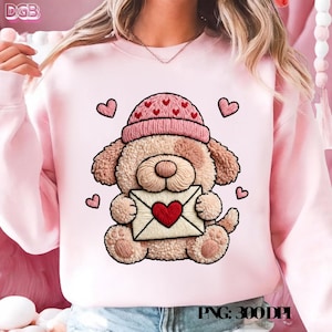 Puede incluir: Sudadera rosa claro con un diseño bordado de un perro que lleva un gorro rosa con corazones. El perro sostiene un sobre con un corazón rojo. Pequeños corazones rosas están dispersos alrededor del perro. El texto "PNG: 300DPI" está en la parte inferior.