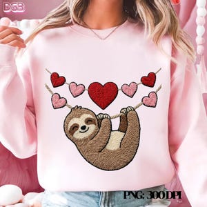 Puede incluir: Sudadera rosa claro con un bordado de un perezoso colgado de una cuerda adornada con corazones rojos y rosas. El perezoso es marrón y beige. El texto "PNG: 300DPI" está en la parte inferior.