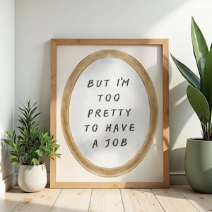 May include: A framed print with the text "BUT I'M TOO PRETTY TO HAVE A JOB" in black lettering. The print has a light brown wooden frame and an oval-shaped design in the center. Two potted plants are on either side of the frame.
