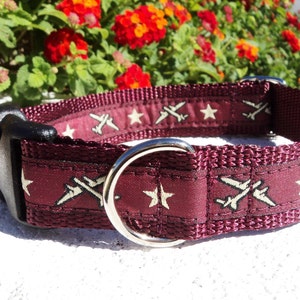 May include: A maroon dog collar with a white star and airplane design. The collar has a black plastic buckle and a silver metal D-ring.