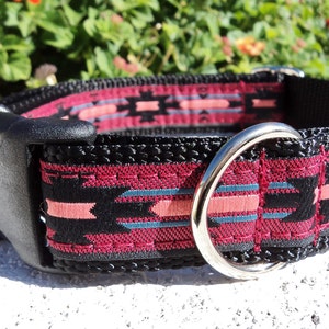 Pu&ograve; includere: Un collare per cani nero con un motivo geometrico rosa e blu. Il collare ha una fibbia in plastica nera e un anello a D in metallo argentato.
