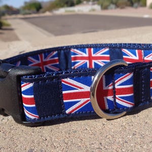 May include: A blue dog collar with a repeating pattern of the Union Jack flag. The collar has a black plastic buckle and a silver D-ring.