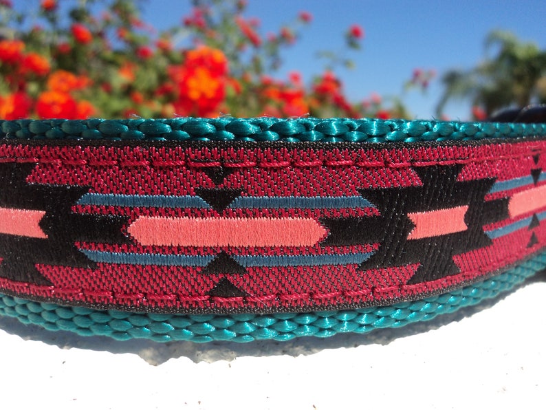 Pu&ograve; includere: Primo piano di un collare per cani in tessuto intrecciato con un motivo turchese, nero, rosa e rosso. Il collare ha un bordo cucito.