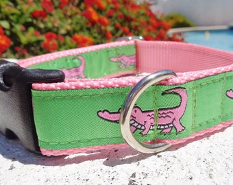 May include: A green and pink dog collar with a black buckle and a silver D-ring. The collar has a repeating pattern of pink alligators on a green background.