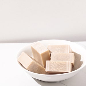 May include: A white ceramic bowl filled with four rectangular bars of beige soap.