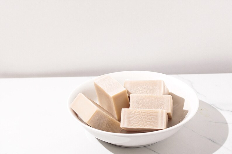 May include: A white ceramic bowl filled with four rectangular bars of beige soap.
