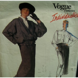 May include: Vogue Patterns Individualist fashion sewing pattern. The pattern features a woman wearing a dark gray jacket, skirt, black hat, and gloves. A sketch of a man in a white shirt and dark pants is also shown. The Vogue logo is at the top.