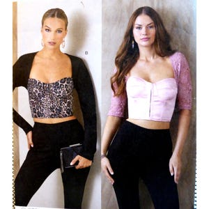 May include: Two women modeling different bustier tops. One wears a leopard print bustier with a black bolero and black pants, holding a black clutch. The other wears a pink bustier with lace sleeves and black pants.
