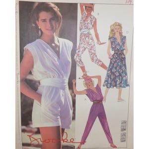 May include: A vintage fashion pattern featuring a woman in a white romper with a wrap-style top and a belted waist. Additional designs include a floral jumpsuit, a blue floral dress, and a purple jumpsuit. The pattern is labeled "Brooke".