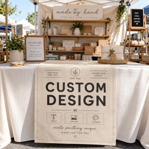 May include: A beige linen table runner featuring black printed text that reads CUSTOM DESIGN, along with icons for text, photos, and colors. The runner includes instructions to add your own text and choose your layout, with a small heart icon at the bottom.
