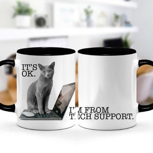 May include: Two white coffee mugs with black rims. The mug on the left has a gray cat sitting on a laptop with the text "IT'S OK." The mug on the right has the text "I'M FROM TECH SUPPORT."