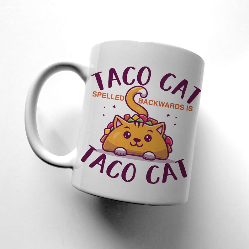 May include: White ceramic mug with a cartoon cat wearing a taco. The text on the mug reads "Taco Cat" and "Spelled backwards is Taco Cat".