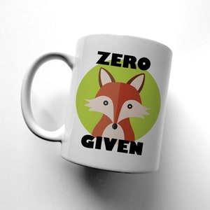 May include: White ceramic mug with a green circle and a cartoon fox with orange fur and black eyes. The text "ZERO GIVEN" is printed in black below the fox.