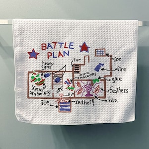 May include: A white kitchen towel with a hand-drawn battle plan on it. The plan includes items like "heavy cans", "tar", "micro machines", "redhot", "ice", "fire", "glue", "feathers", and "fan".