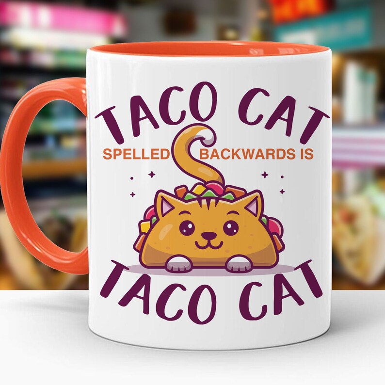 May include: White ceramic coffee mug with an orange rim. The mug features a cartoon cat inside a taco with the text "Taco Cat Spelled Backwards Is Taco Cat".
