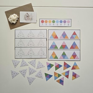 Peut inclure: Matériel pédagogique de style Montessori. L'image présente des formes géométriques colorées et des cartes de nombres. Comprend un spectre de couleurs, des puzzles triangulaires et des cartes d'association de nombres. Une enveloppe marron et une fleur décorative sont également présentes.