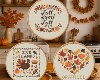May include: Three fall-themed cross-stitch hoops. One reads "Fall Sweet Fall" with leaf accents. Another says "Give Thanks" with a turkey and pumpkin. The third is a heart shape with "Gratitude" and fall leaves.