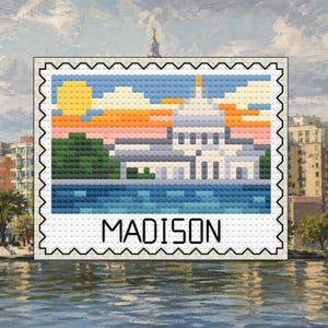 May include: A cross-stitch design of a domed building, like a capitol, against a sunset sky. The word "MADISON" is below the building within a postage stamp border. The background shows water and buildings. The design is reminiscent of a postage stamp.