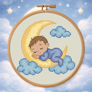 Puede incluir: Bordado de punto de cruz en un aro de madera. El diseño presenta a un bebé durmiendo en pijama azul descansando sobre una luna creciente amarilla, rodeado de nubes azules. El fondo es un cielo azul con estrellas.