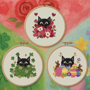 Op de afbeelding: Drie borduurringen met zwarte kattenontwerpen. Eén kat is omringd door roze bloemen en harten, een andere door groene klavers en de derde door paaseieren en konijntjes. De ringen staan op een kleurrijke, geschilderde achtergrond.