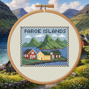 Puede incluir: Un bastidor de bordado de punto de cruz con un paisaje pixelado de las Islas Feroe. El diseño incluye montañas verdes, agua azul y casas coloridas. El texto "FAROE ISLANDS" está bordado en la parte superior.
