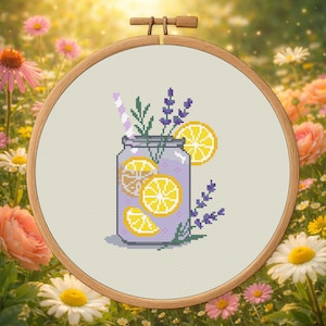 May include: Cross-stitch embroidery of a purple jar filled with lemonade and lemon slices, a striped straw, and sprigs of lavender. The embroidery is set in a wooden hoop, with a background of flowers.