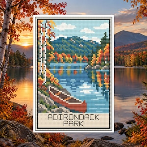 May include: A cross-stitch pattern featuring a landscape of Adirondack Park with a red canoe on a blue lake, surrounded by autumn trees and mountains. The text ADIRONDACK PARK is printed in black at the bottom of the rectangular design.