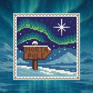 May include: Cross-stitch design featuring a winter scene with the text "NORTH POLE" on a signpost. The background shows the aurora borealis, a star, and snow-covered terrain. The design is framed with a decorative border.