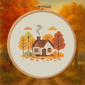 Può includere: Un telaio da ricamo a punto croce con una scena autunnale accogliente. Il disegno raffigura una piccola casa con un camino fumante, circondata da alberi nei toni dell'arancione, giallo e marrone. Il telaio è in legno.