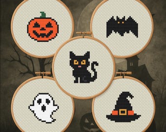 May include: Five cross-stitch embroidery hoops with Halloween-themed designs. The designs include a jack-o'-lantern, a bat, a black cat, a ghost, and a witch's hat. Each design is stitched on a light beige fabric and set in a wooden hoop.