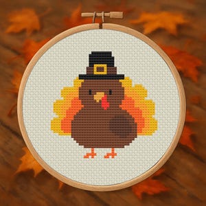 May include: A cross-stitch design of a turkey wearing a black pilgrim hat with a gold buckle. The turkey has brown feathers and a red wattle. The design is set in a wooden embroidery hoop.