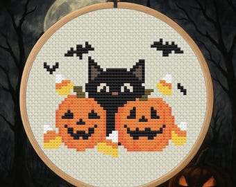 May include: A cross-stitch embroidery in a wooden hoop features a black cat between two orange jack-o'-lanterns. Candy corn and bats are scattered around the cat and pumpkins. The background is a dark, spooky scene with a full moon.