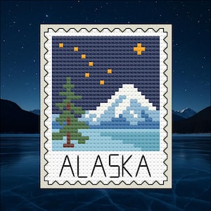 Può includere: Design a punto croce raffigurante un paesaggio dell'Alaska. L'immagine mostra una catena montuosa, un pino e uno specchio d'acqua sotto un cielo stellato. La parola "ALASKA" è scritta in grassetto nella parte inferiore del design.