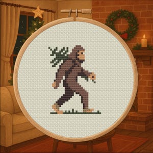 May include: Cross-stitch embroidery in a wooden hoop depicts a brown Bigfoot carrying a Christmas tree branch. The design is set against a cream-colored background, with a green grass line at the bottom. The scene is set in a cozy room with a fireplace and Christmas decorations.