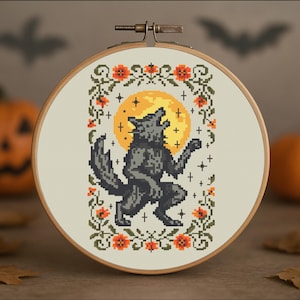 Puede incluir: Un bastidor de bordado de punto de cruz con un hombre lobo aullando bajo la luna llena. El diseño incluye flores naranjas y vides verdes, en un aro de madera. El fondo tiene un tema de Halloween con calabazas y siluetas de murciélagos.