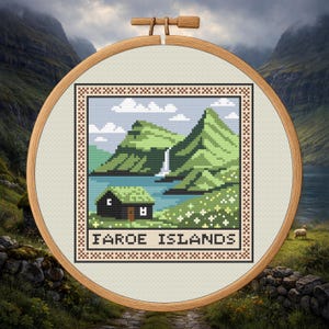 Puede incluir: Bordado de punto de cruz de las Islas Feroe, con una pequeña cabaña con tejado verde, una cascada y colinas verdes. El texto "FAROE ISLANDS" está bordado en la parte inferior. El bordado está en un bastidor de madera.
