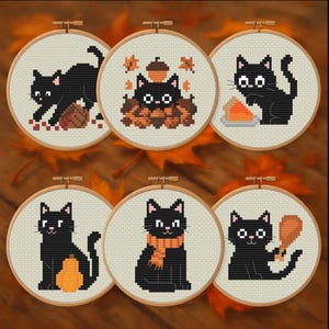 May include: Six cross-stitch embroidery hoops featuring black cats in various autumnal scenes. The cats are depicted with pumpkins, pie, and fall leaves. The hoops are displayed on a wooden surface with fall leaves.