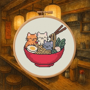 May include: Cross-stitch embroidery of a red bowl of ramen with three cartoon cats, chopsticks, and an egg. The embroidery is set in a wooden hoop, with a background of a Japanese restaurant.