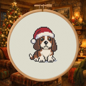 Könnte beinhalten: Kreuzstich eines Cavalier King Charles Spaniel Welpen mit Weihnachtsmütze. Der Hund ist braun, weiß und schwarz, mit roter und weißer Mütze. Der Kreuzstich befindet sich in einem hölzernen Stickrahmen, ideal für Weihnachtsdekoration.